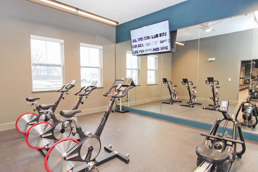 Apartment community fitness center with exercise bikes, glass wall, and flat-screen TV.