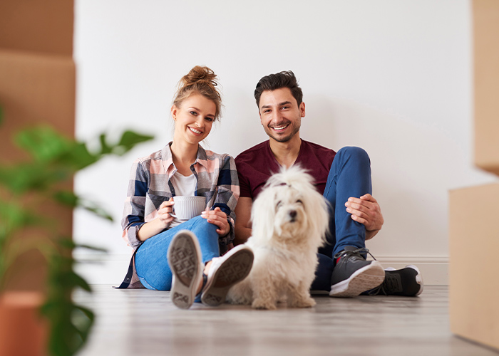 Couple sitting on the floor with a dog and boxes.